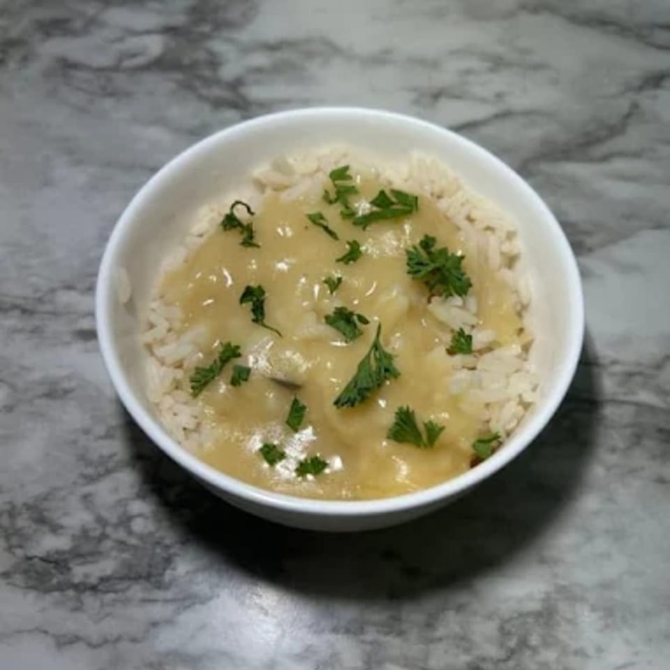 A white bowl of rice topped with creamy gravy and fresh parsley on a marble surface.