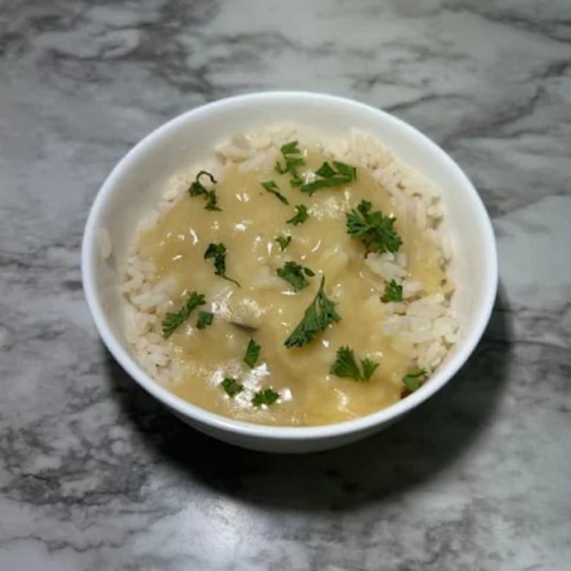 A white bowl of rice topped with creamy gravy and fresh parsley on a marble surface.