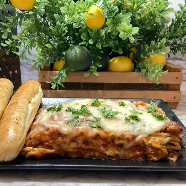 A generous serving of Deja Soul's lasagna with melted cheese and fresh parsley, alongside two breadsticks.