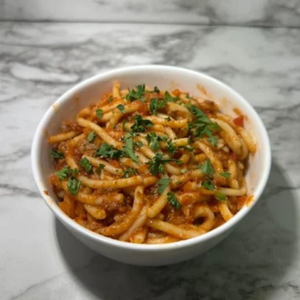A white bowl filled with Deja Soul's spaghetti, topped with a rich red sauce and fresh parsley.