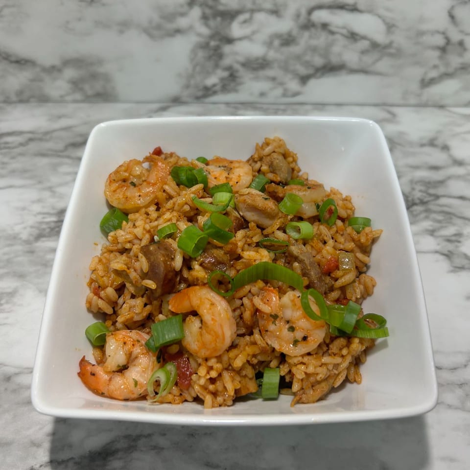 A white square bowl filled with Deja Soul's jambalaya, garnished with fresh green onions.