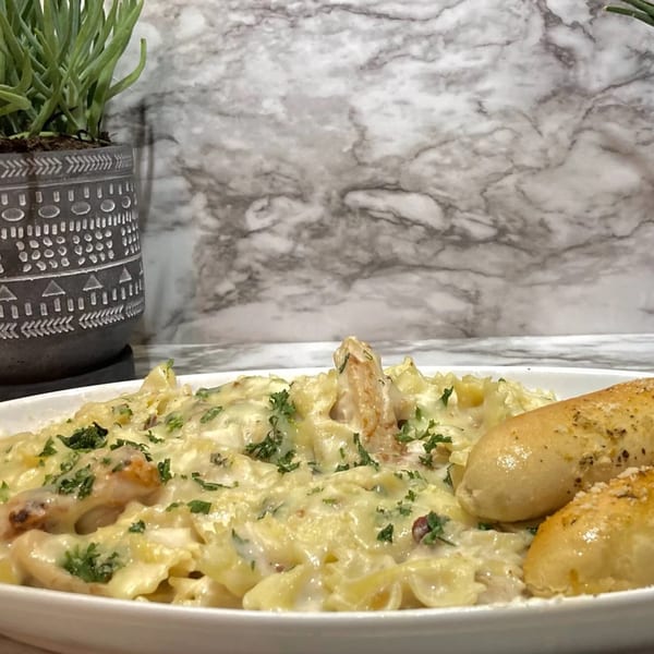 Creamy pasta with chicken and parsley, served with two breadsticks, against a marble background.
